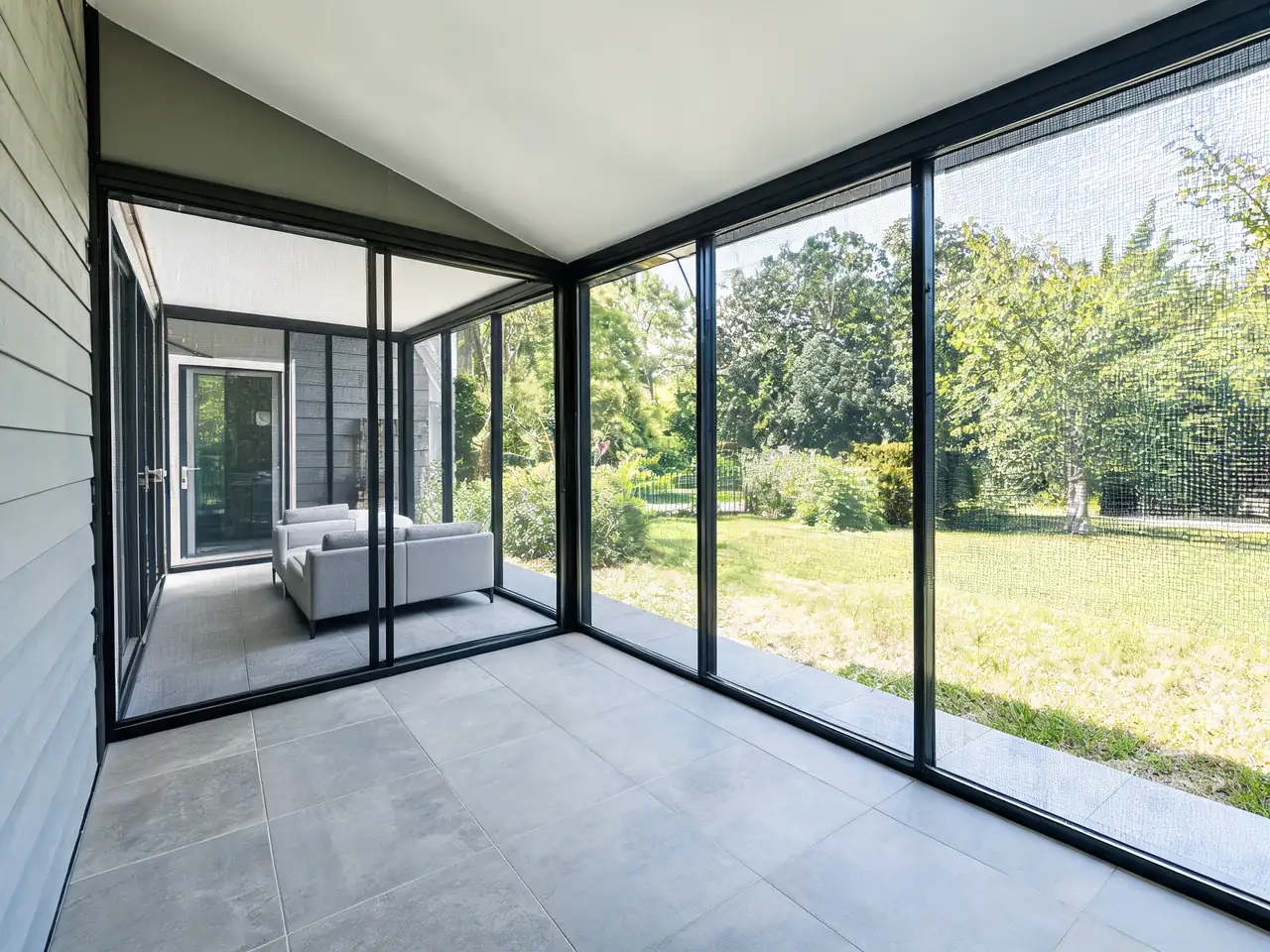 Modern screened-in porch idea with slim black aluminum frames and a low outdoor sofa