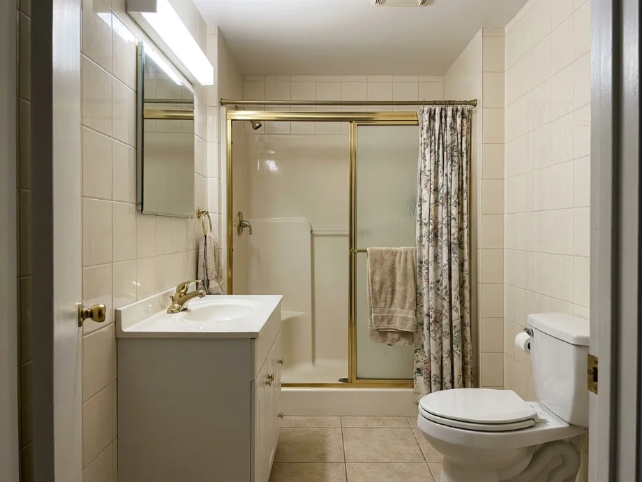 Family bathroom retiled with large-format stone and a frameless glass shower. before AI redesign