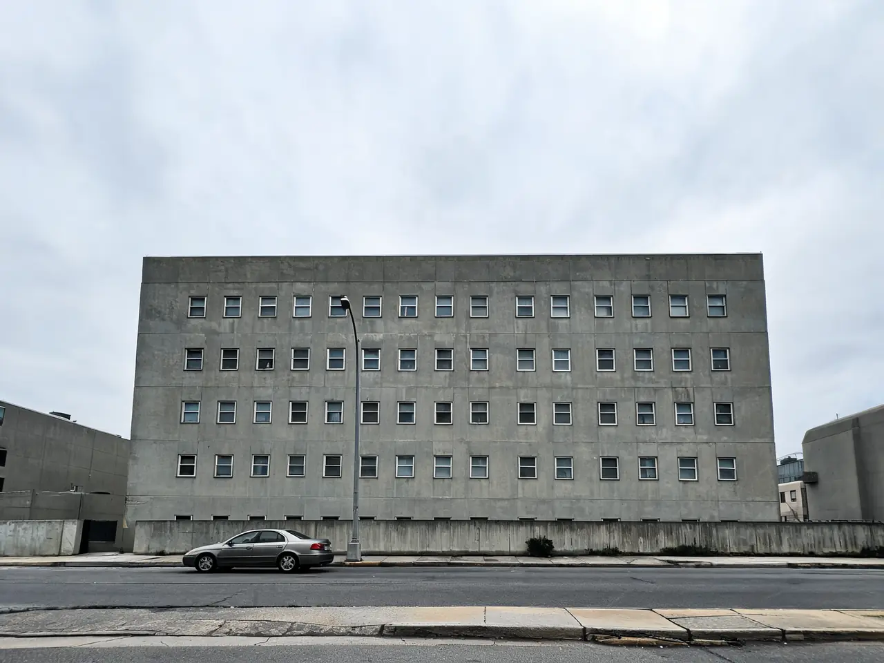 AI facade redesign of a dated concrete office building in glass and timber before AI redesign