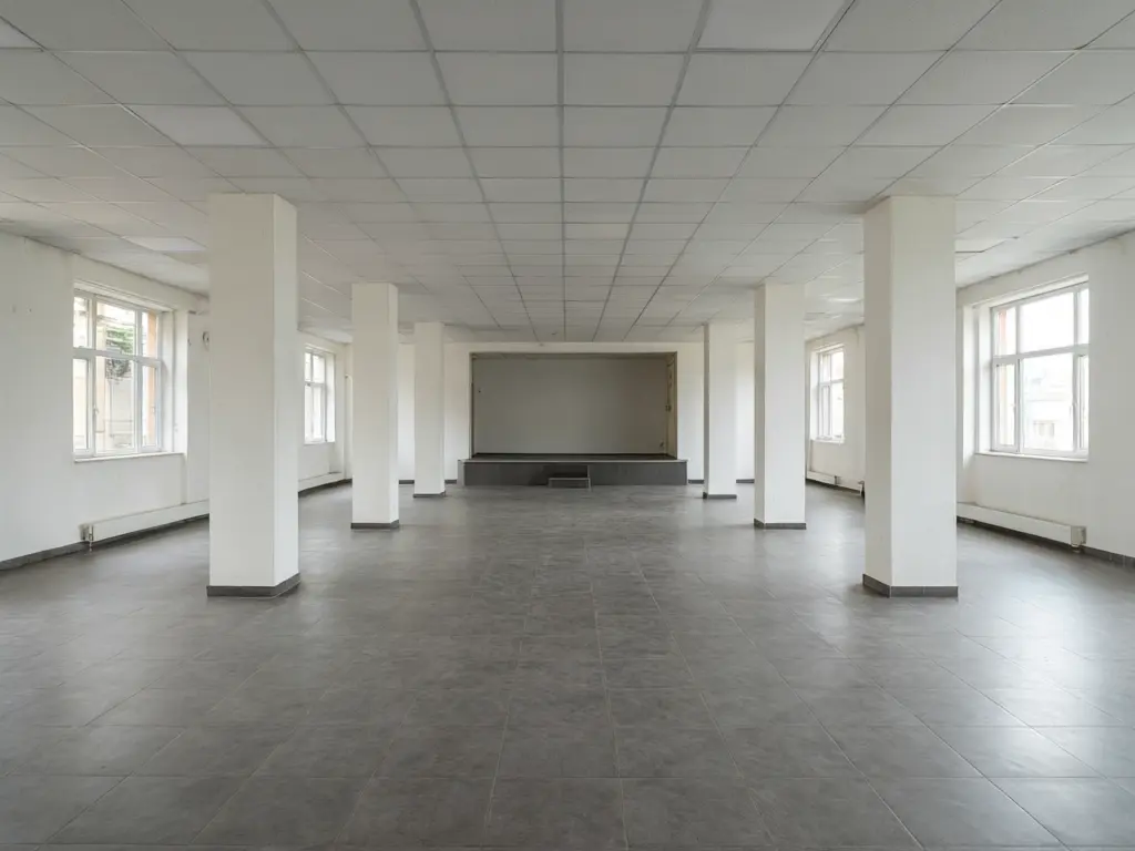 Banquet hall interior design result: empty white hall with square pillars refitted with ivory and gold wall panels, gold wrapped pillars, crystal chandeliers, round tables with white linens and gold chairs, and a white floral stage wall before AI redesign