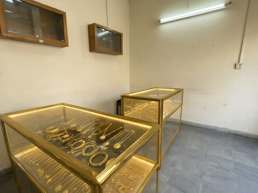 Jewellery counter design result: two old wooden counters in a small gold shop replaced with glass counters with gold trim and warm LED lighting, same positions, gold jewellery on display after AI redesign