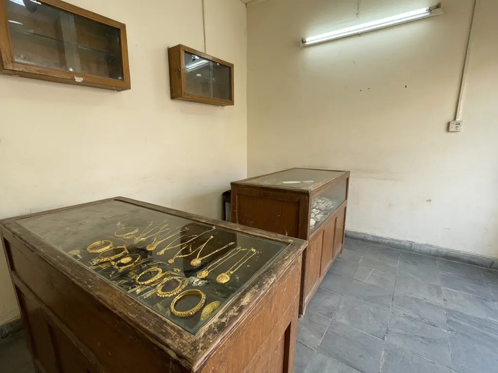Jewellery counter design result: two old wooden counters in a small gold shop replaced with glass counters with gold trim and warm LED lighting, same positions, gold jewellery on display before AI redesign
