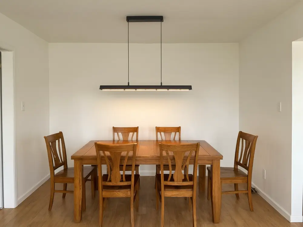 Light fixture visualizer result: a black modern linear chandelier over a dining table after AI redesign